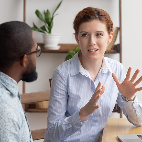 Young adult colleagues talk sitting at a table in an office.