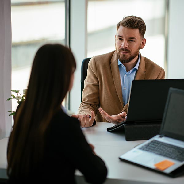 Two businesspeople chatting beside an open laptop in an office.