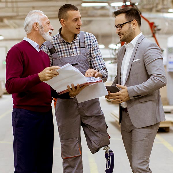 A man with a prosthetic leg talks with two other men in a warehouse.